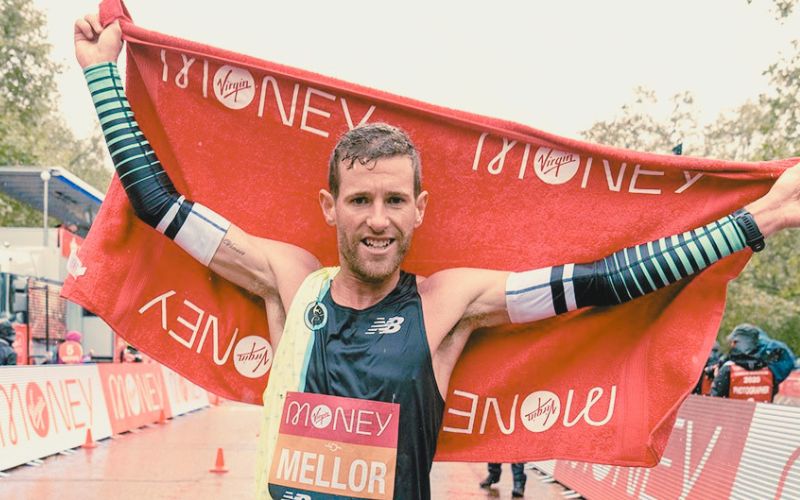 Runner crossing a marathon finish line, arms raised, capturing the emotion behind why people run a marathon